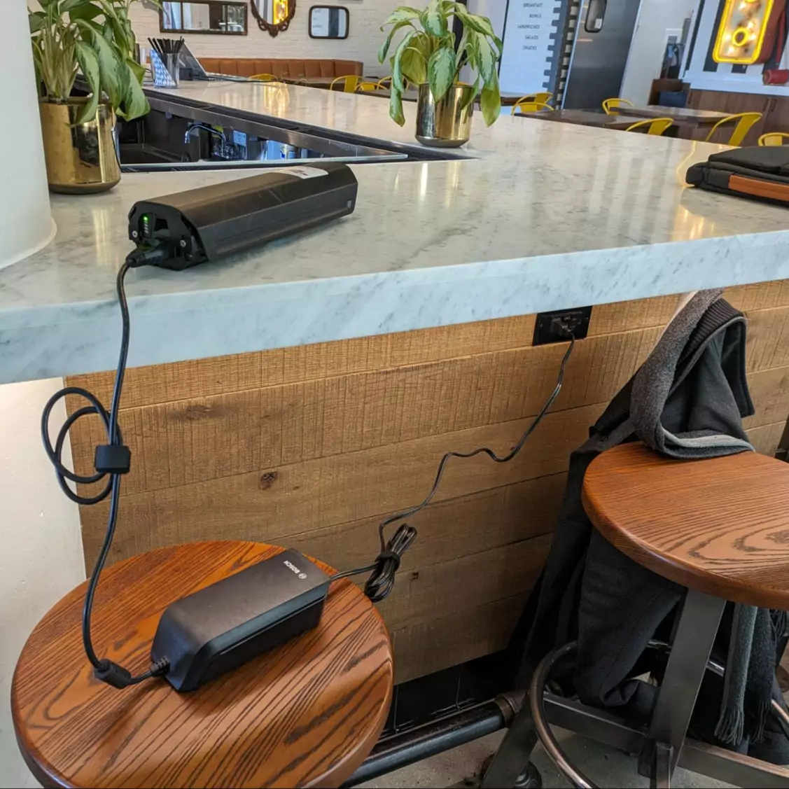 Viktor's e-bike battery on its own, being plugged into the wall at a coffee shop