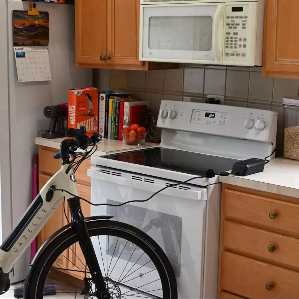 Viktor's white Gazelle e-bike in his kitchen, plugged into the wall behind the stove